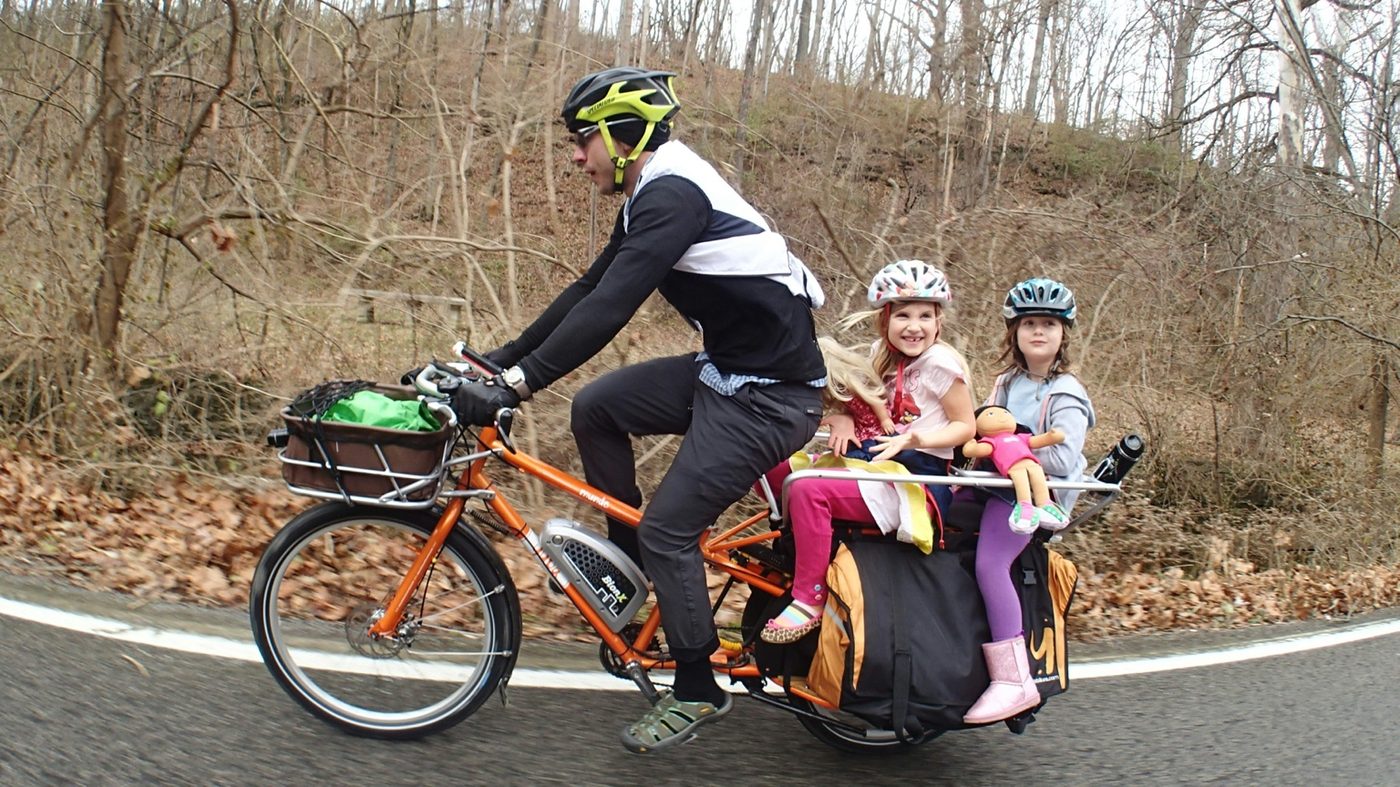 Adult carrying two children on a longtail cargo e-bike with bags