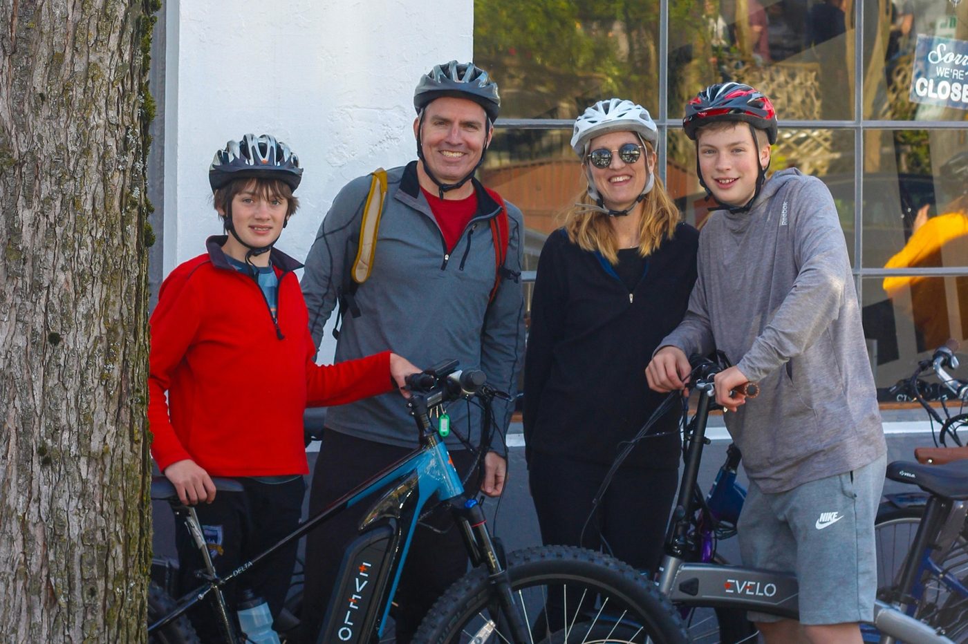 Family of four with helmets standing beside their e-bikes
